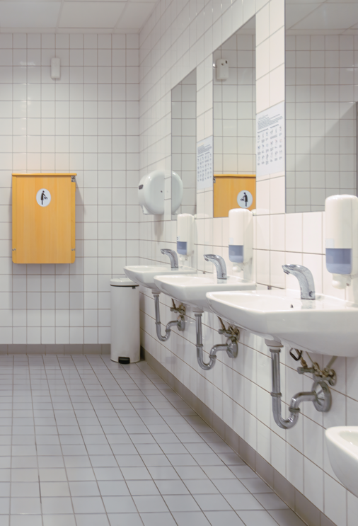 Commercial washroom with tiled walls, mirrors and row of sinks.