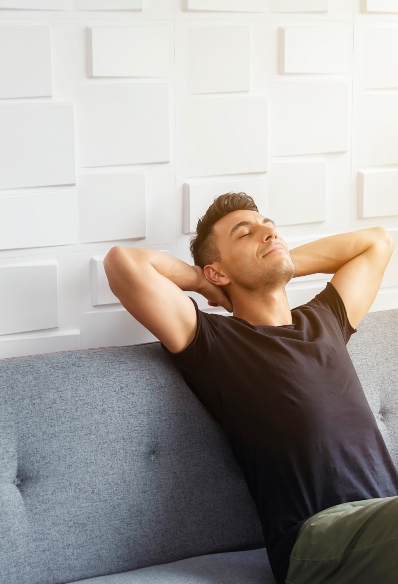 A young man sitting back and relaxing on a sofa with hands behind his head